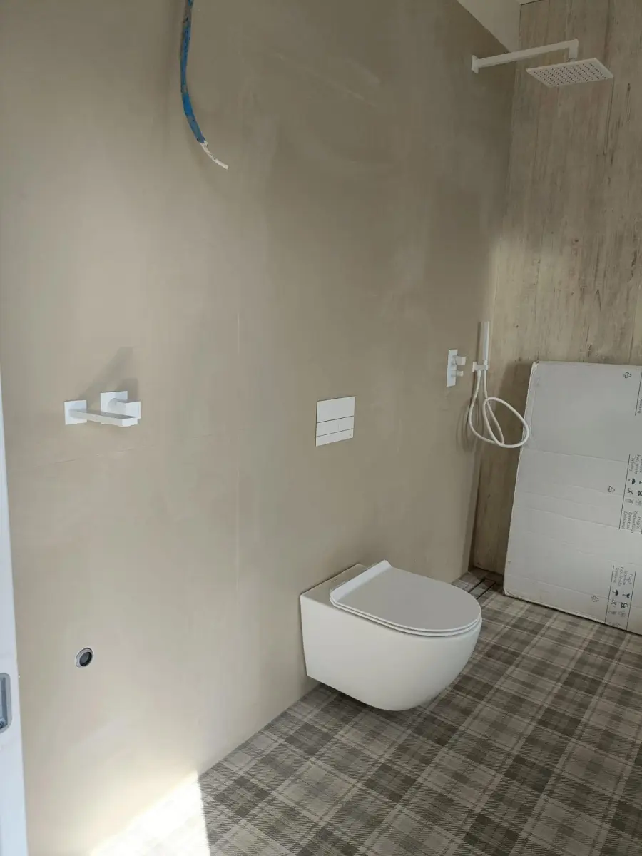 Vas de WC suspendat cu rezervor încastrat și duș de tavan, într-o baie în curs de finisare